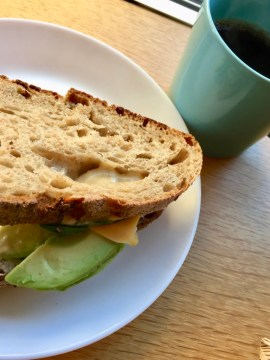 Smörgås med avokad och ost på vitt fat, till höger en grön kaffekopp med svart kaffe i